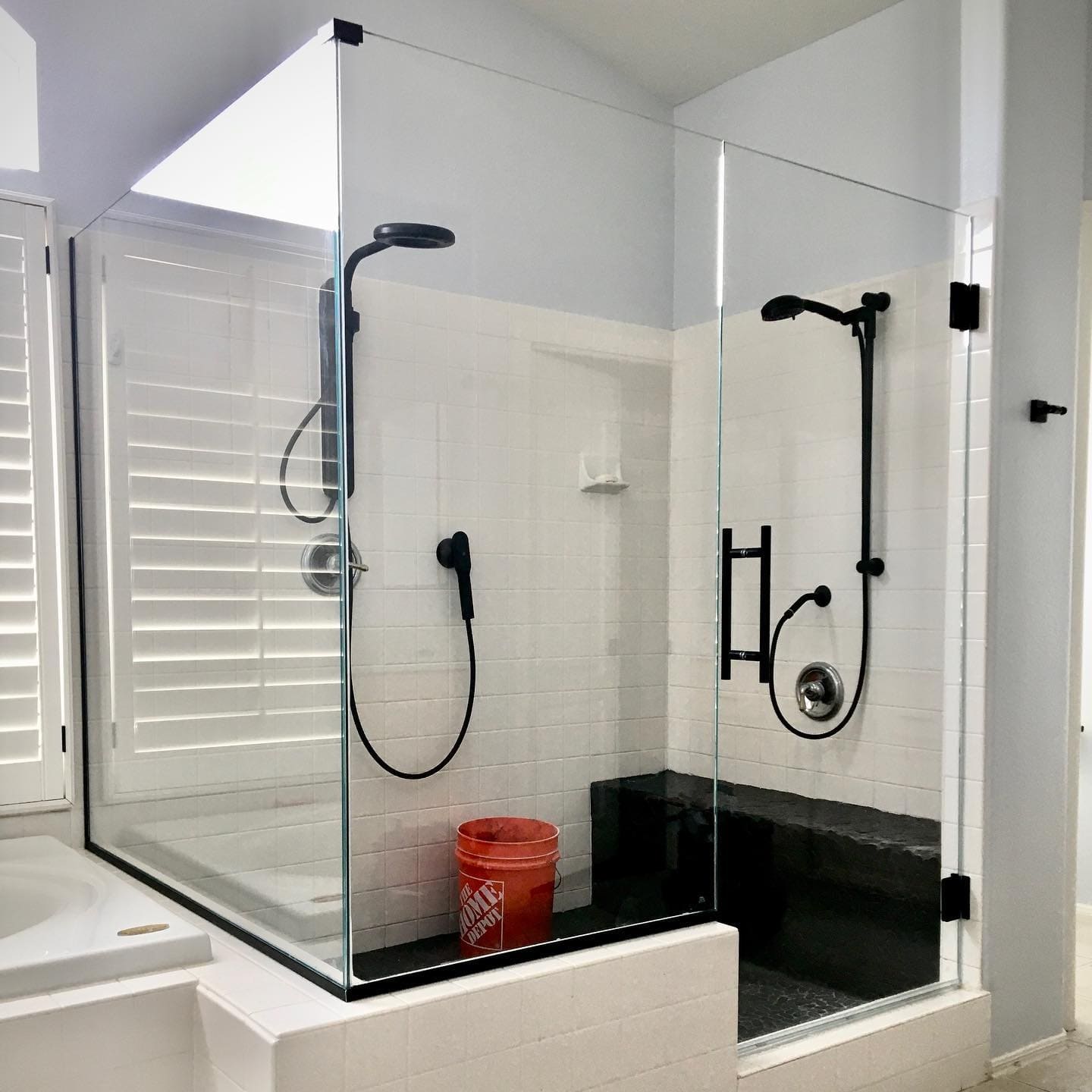 Custom corner glass shower enclosure with matte black hardware and dual showerheads installed in a Las Vegas home bathroom
