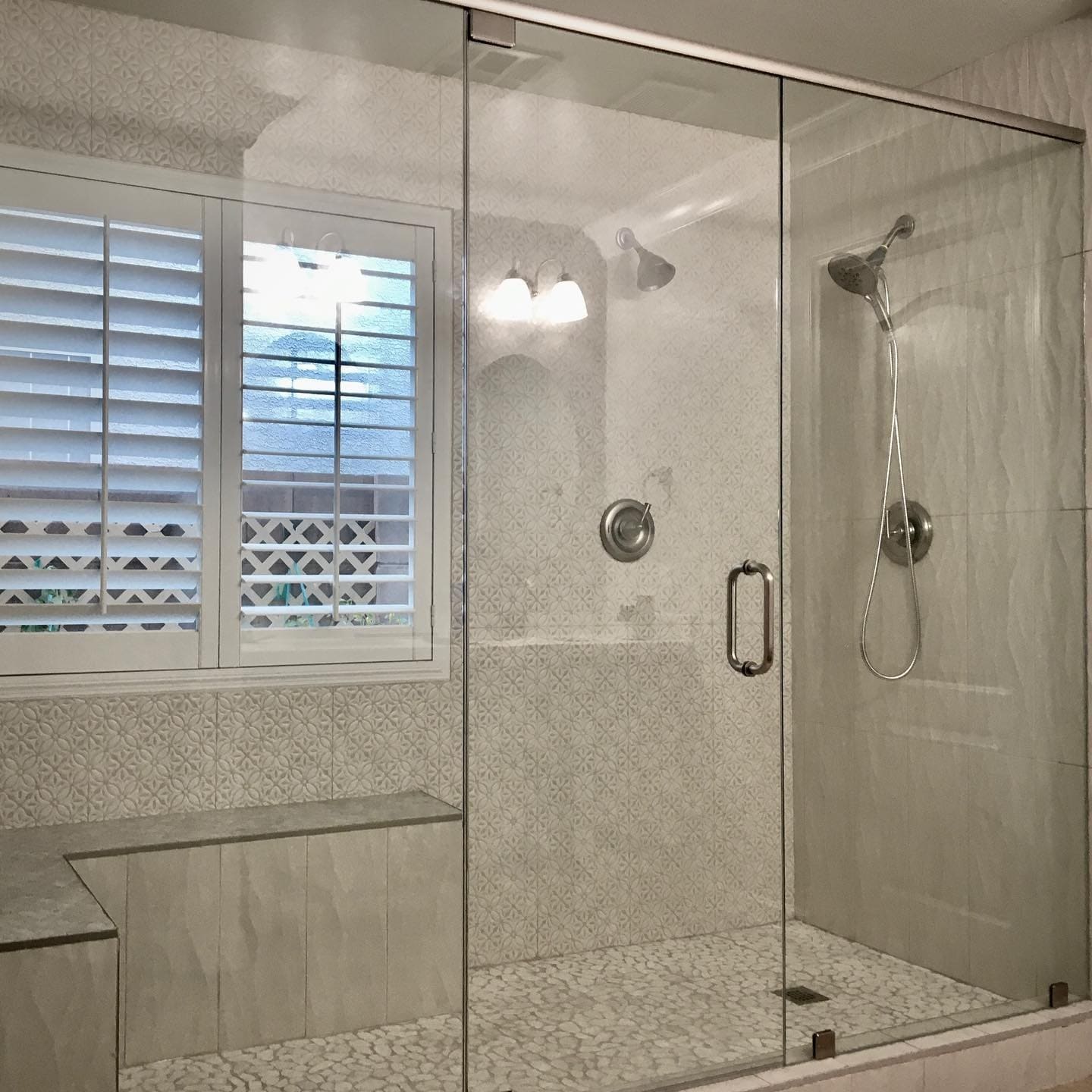 Frameless walk-in glass shower enclosure with built-in bench seat and decorative tile pattern in a Summerlin NV master bathroom