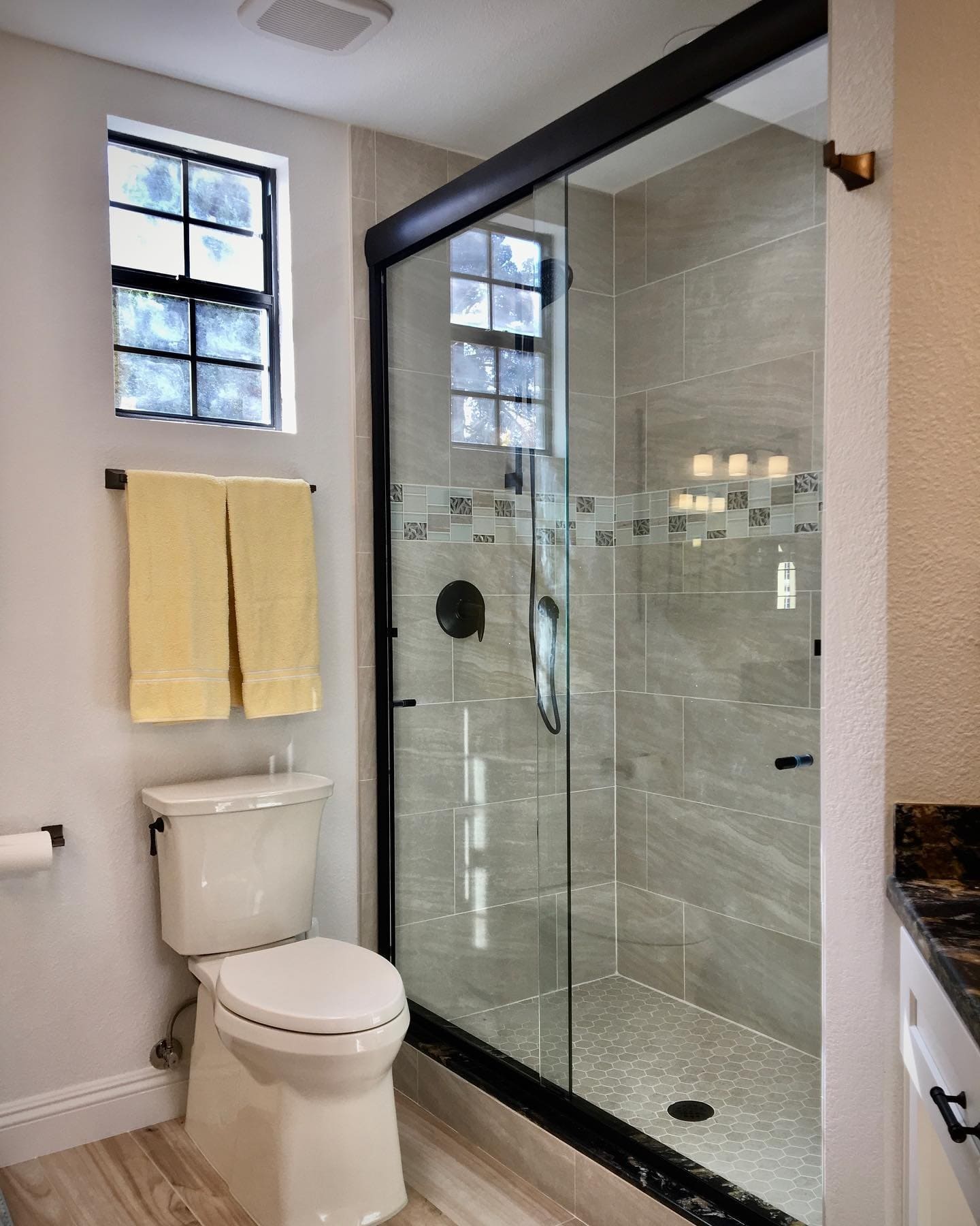 Semi-frameless corner shower enclosure with oil-rubbed bronze hardware and decorative tile accent band in a Las Vegas home