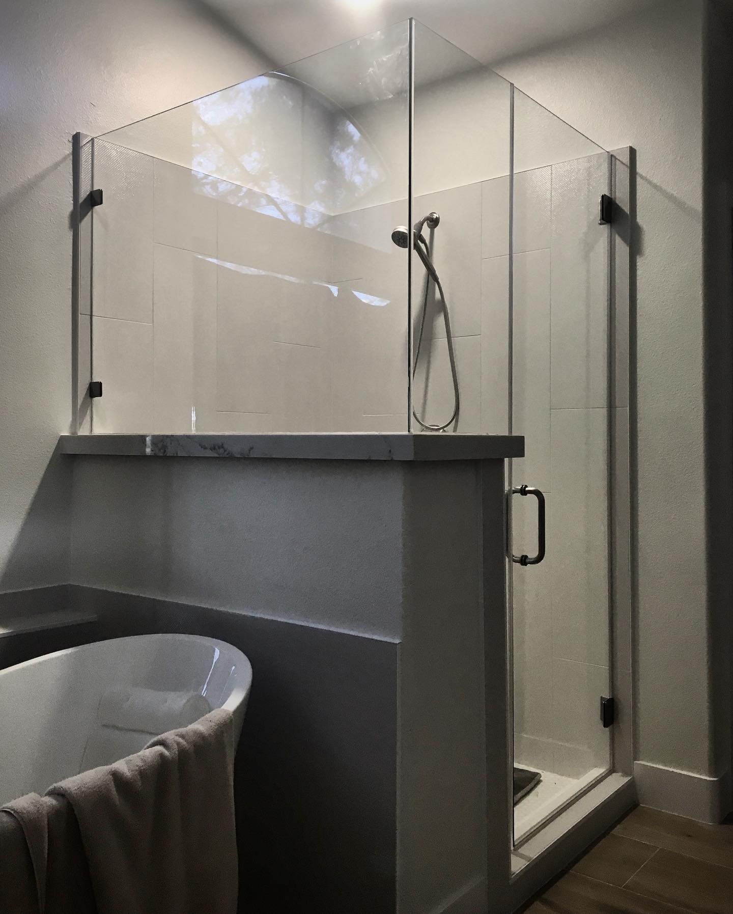 Clear 10mm frameless shower door installed above a half wall with brushed nickel handle in a Henderson NV bathroom with freestanding tub