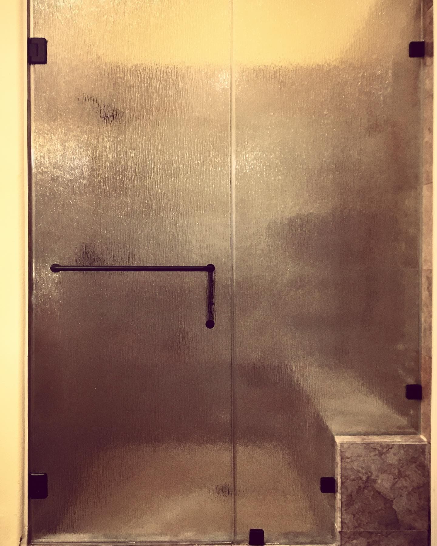 Rain textured glass frameless shower door with matte black square clips and towel bar installed in a Henderson NV guest bathroom
