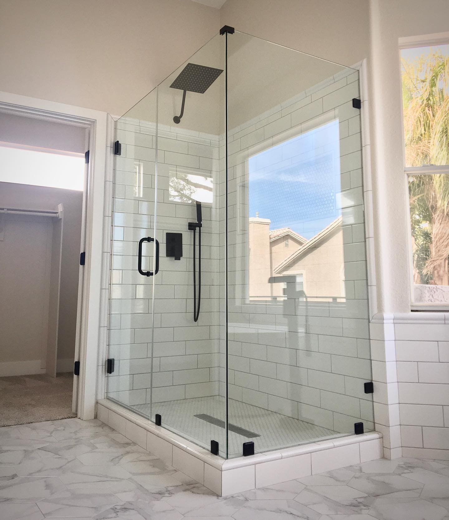 Frameless glass shower door with matte black hinges and rain showerhead installed in a Las Vegas master bathroom with white subway tile