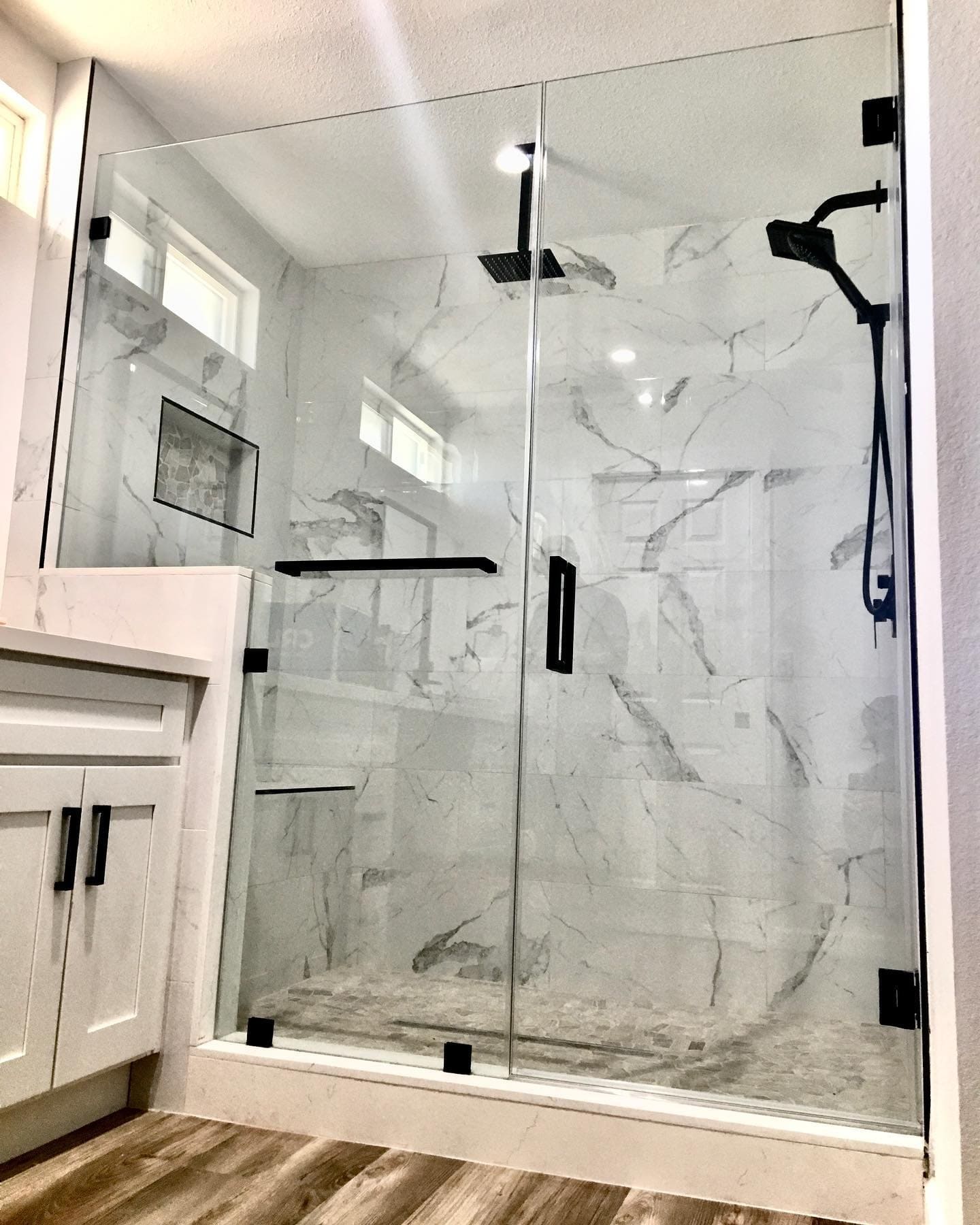Frameless glass shower door with matte black hardware on a marble tile surround with built-in niche installed in a Summerlin NV home