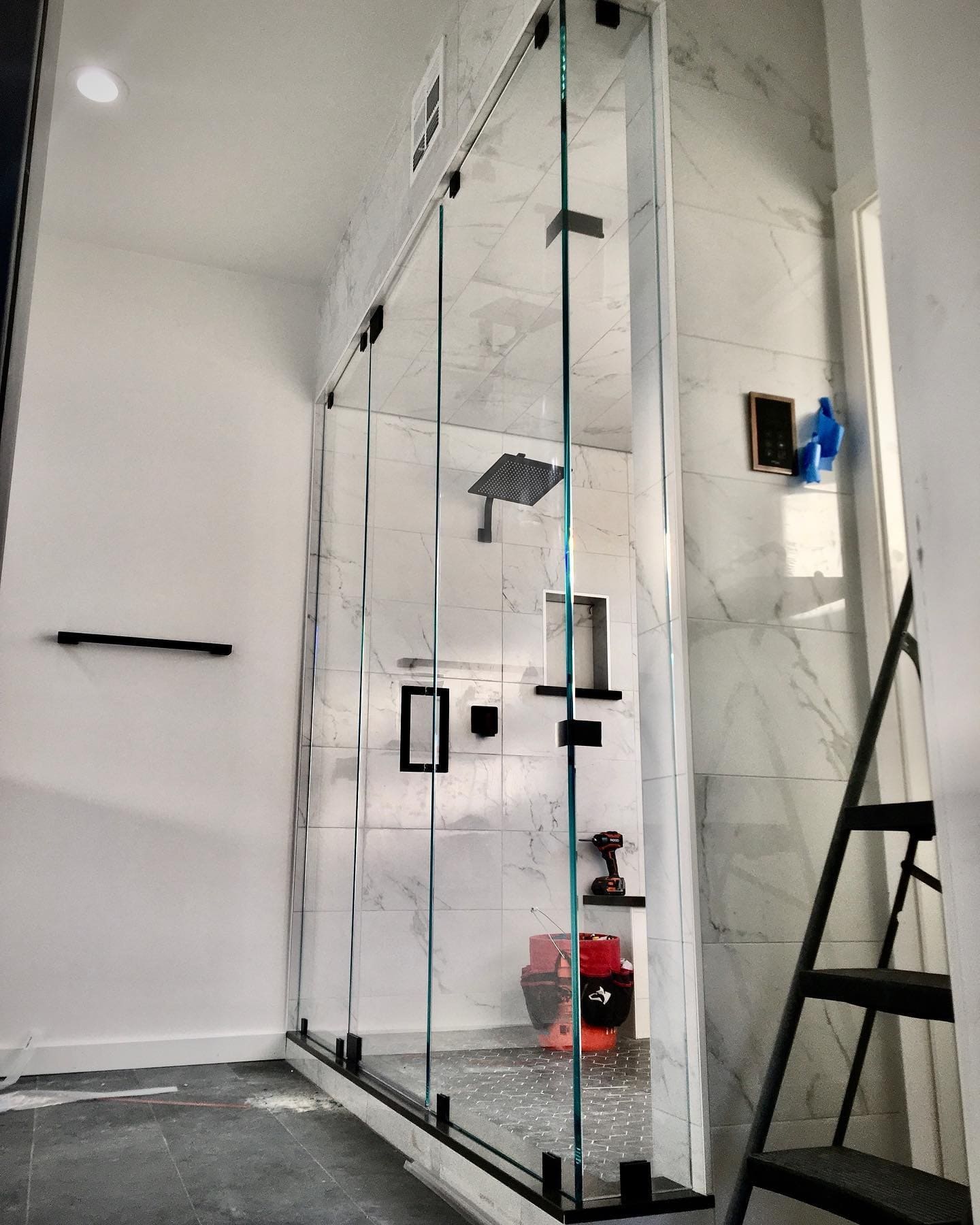Floor-to-ceiling frameless glass shower door with matte black hardware and marble tile walls installed in a new Las Vegas home build